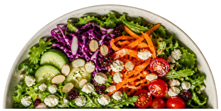 Half of a white plate filled with mixed greens, halves of cherry tomatoes, feta crumbles, shredded carrots, and shredded cabbage